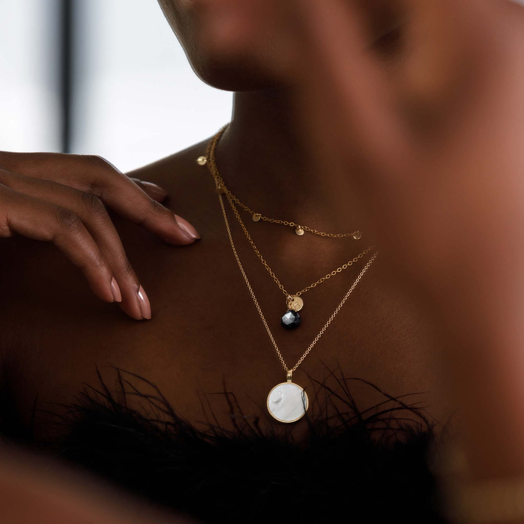 An iridescent black mother of pearl in our signature faceted shape floats delicately on a fine gold chain. Personalise your necklace with a 14k gold fill initial charm, hand stamped and made to order.