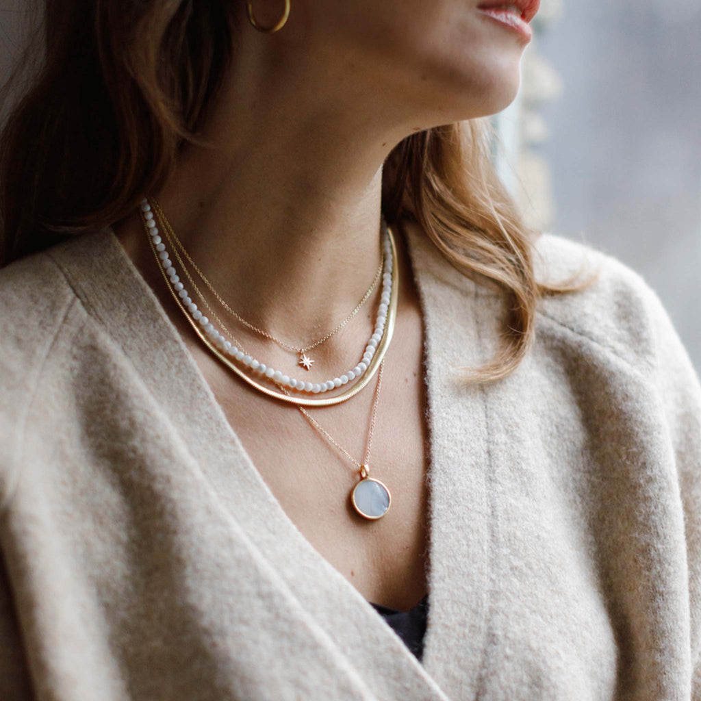 The Mother of Pearl Porthole Necklace styled with the Paseo Herringbone Snake Chain and Kai gemstone necklace with the Nova Star Necklace.