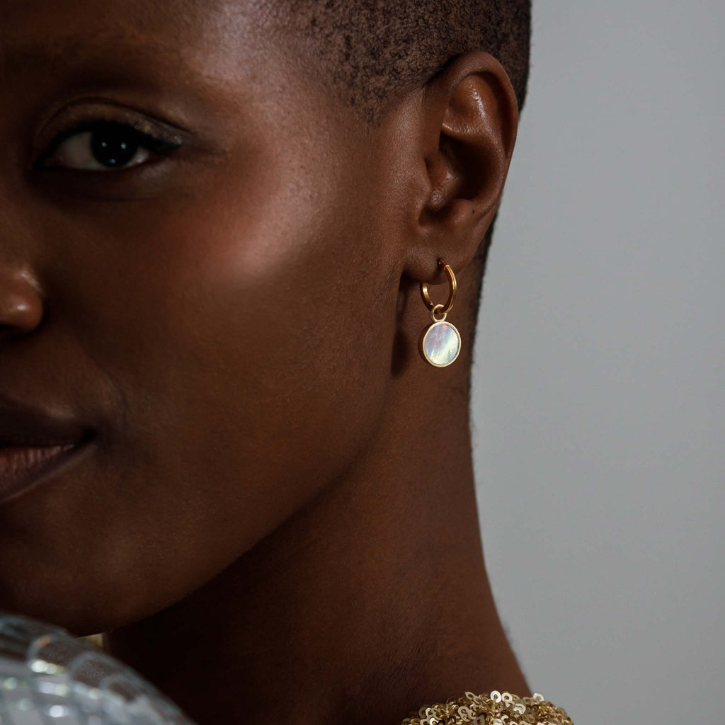 A circle of subtle brushed gold surrounds a mother of pearl slice, reminiscent of light flooding through a porthole. 18k Gold Vermeil charm hoop earrings, designed in Devon.