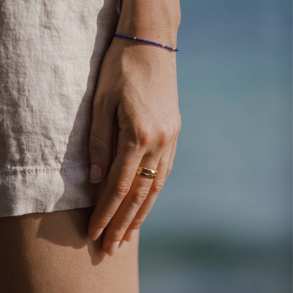 Two gold vermeil faceted band rings are worn stacked together on the middle finger. Styled with a cobalt blue and gold minimal beaded bracelet.