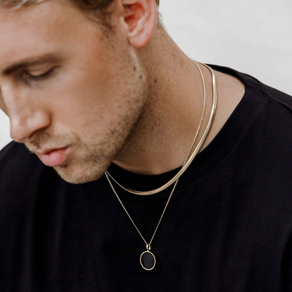 Max Wears the Paseo Herringbone Necklace, a timeless and iconic wide snake chain; styled with the Black Onyx Gemstone Porthole Necklace. Shop meaningful jewellery, designed in the UK by Wanderlust Life.