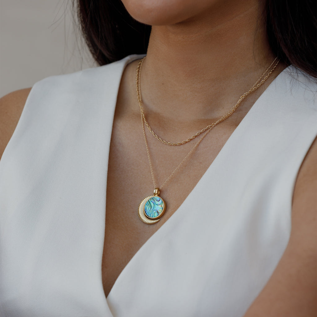 A Porthole Necklace with a circular slice of Paua shell, framed in brushed gold vermeil pendant. Styled with a mother of pearl beaded necklace.