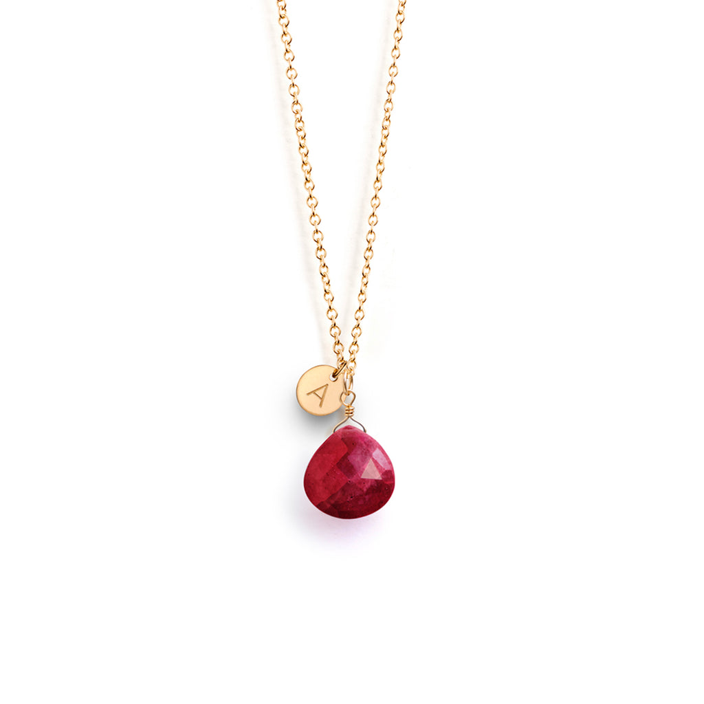 A ruby gemstone floats on a minimal gold fill chain. This birthstone necklace is personalised with a circular charm, hand-stamped with an A initial.