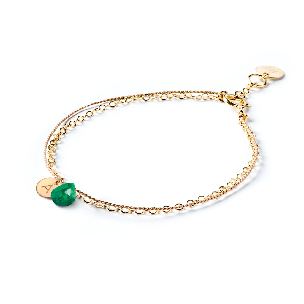 May Birthstone Bracelet personalised with an initial tag. Choose your initial and our jewellery maker’s personalise your birthstone bracelet. The bracelet creates the appearance of two individual bracelets layered into a stack, but the bracelet combines a layer of silk with a fine gold chain, decorated with an emerald gemstone in our signature faceted style. 