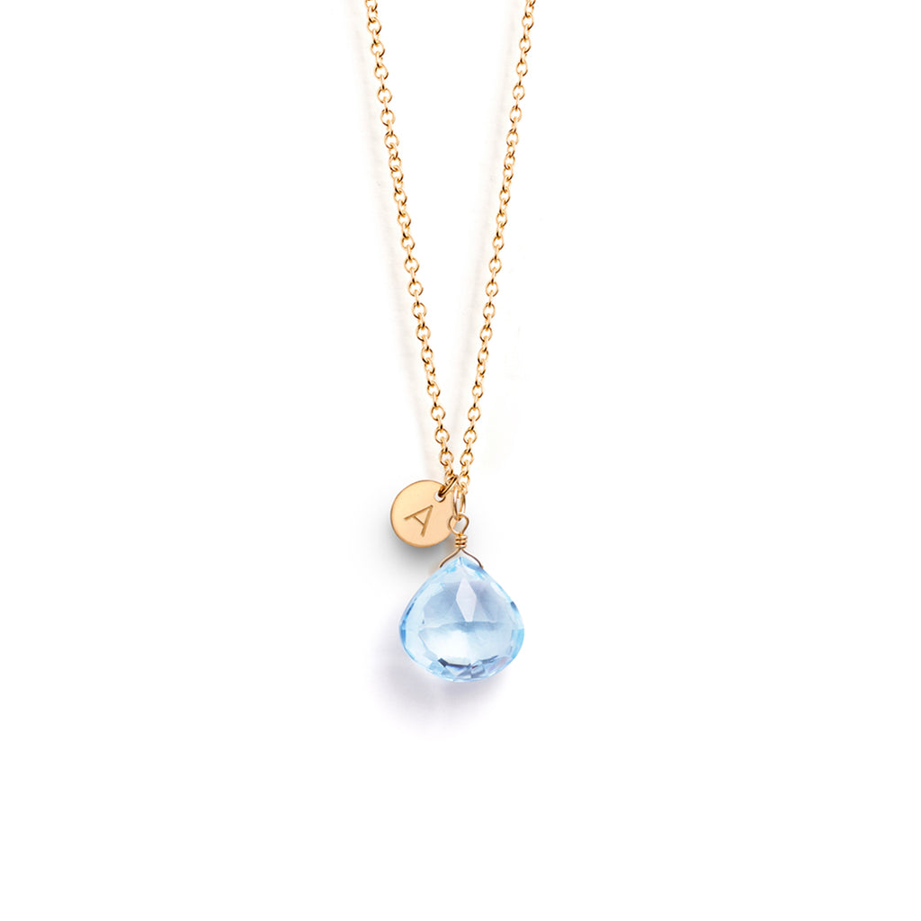 A November birthstone pendant necklace features a blue topaz gemstone in our signature faceted shape. This birthstone necklace is personalised with a gold initial charm, hand-stamped with an A.