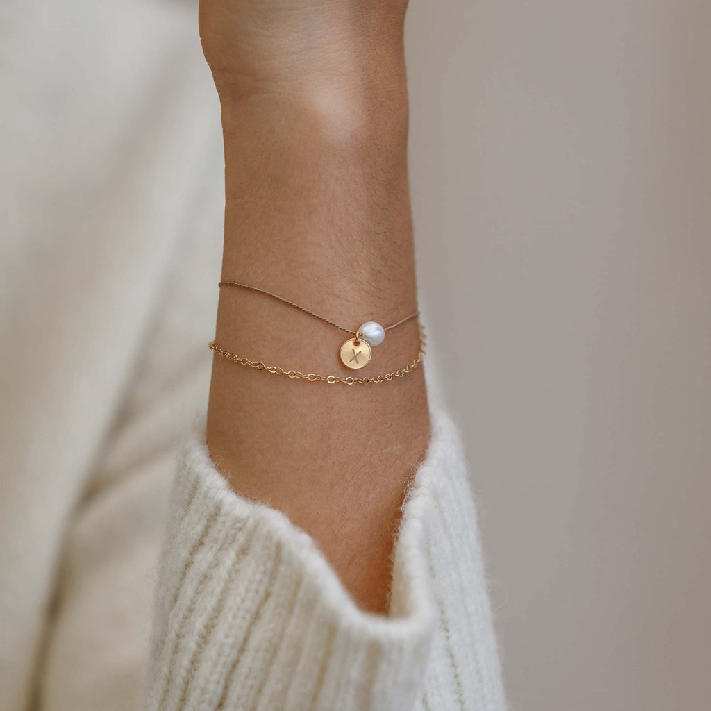 Personalised with a tag charm with the letter x, symbolic of a kiss. This bracelet features a freshwater pearl on silk, doubled up with a fine gold-fill chain. This bracelet creates the illusion of two bracelets stacked together. Shop personalised pearl jewellery.