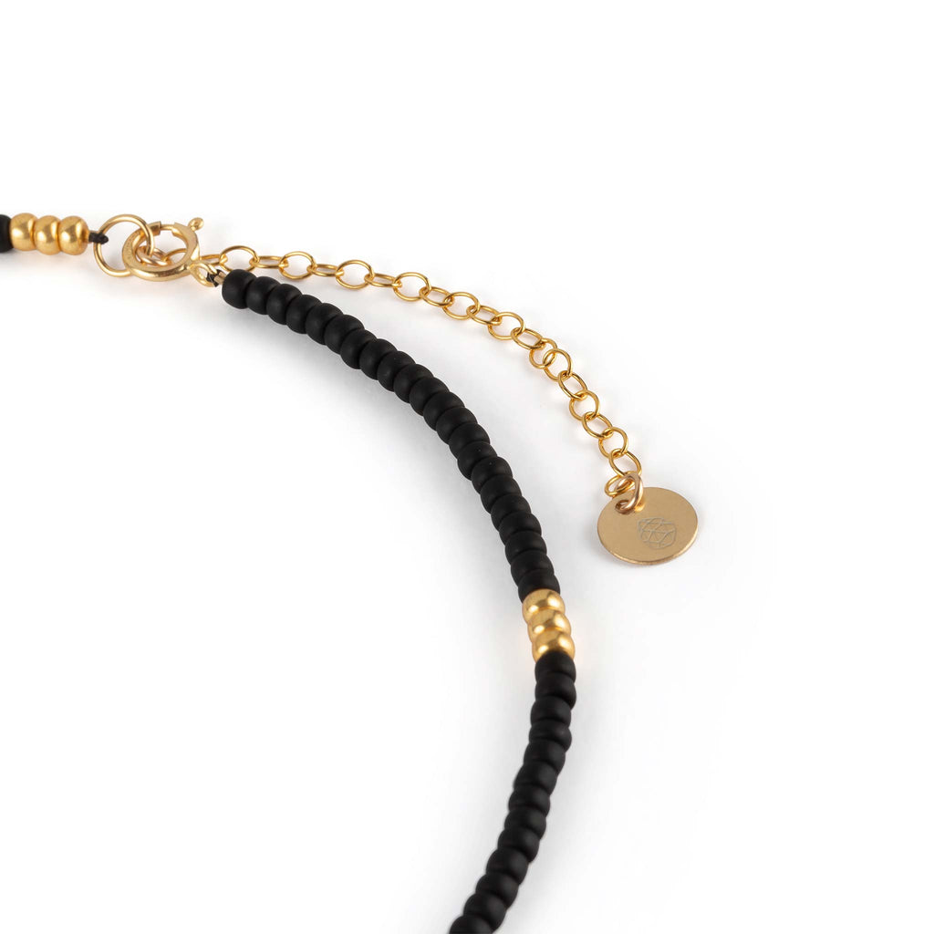 The Poolside Noir Beaded Necklace in black and gold features 2 inches of adjuster chain, making it adjustable and effortless to style with other necklaces. The necklace is finished with a branded hand-stamped Wanderlust Life tag.