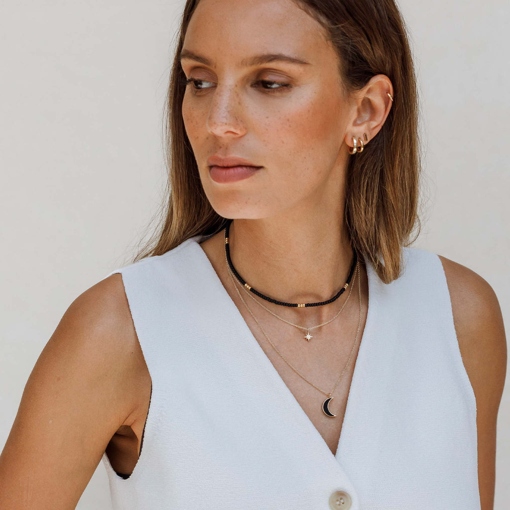 The Petite Nova Necklace features a golden star pendant on a minimal and adjustable 14k gold fill chain. Perfect for layering, the celestial necklace is worn layered with a black beaded necklace and black onyx moon pendant.