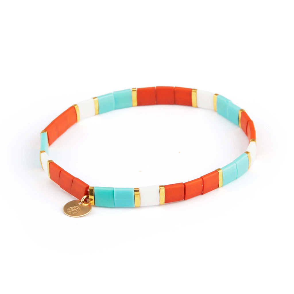 The Safi Layering Bracelet is an elasticated beaded bracelet, featuring a pattern of burnt orange, turquoise, white and gold tila beads and a branded Wanderlust Life charm.