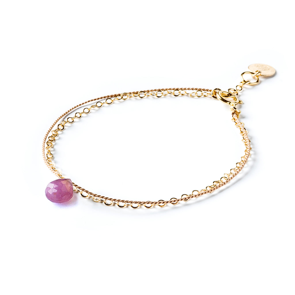 September Birthstone Bracelet with pink sapphire gemstone. A layer of silk is decorated with the September birthstone, combined with a layer of fine gold chain, this bracelet creates the look of two bracelets layered into a stack. Shop minimal, modern and meaningful birthstone jewellery.
