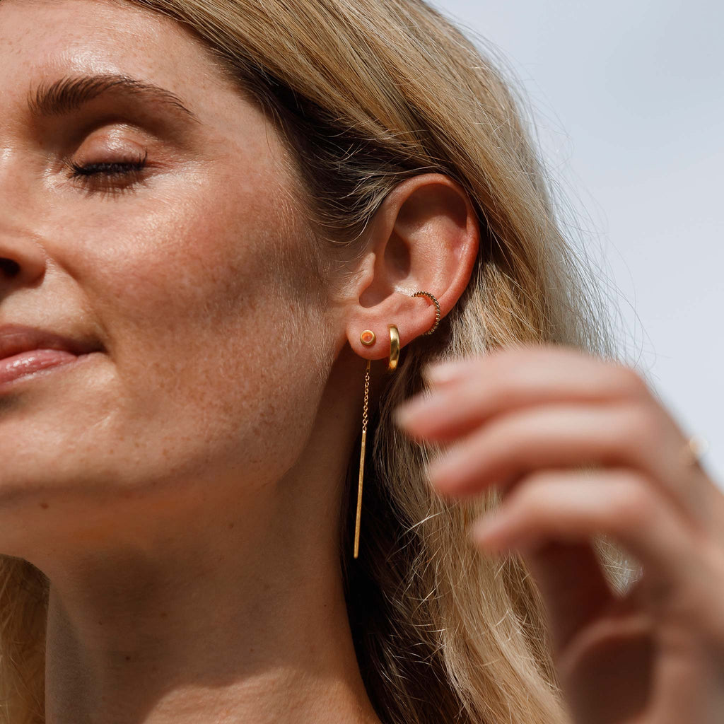 The Solstice Ear cuff is formed of miniature orbs that create a textured yet minimal golden ear cuff. It's styled here in an ear stack with statement threader chain earrings and a huggie hoop earring. 