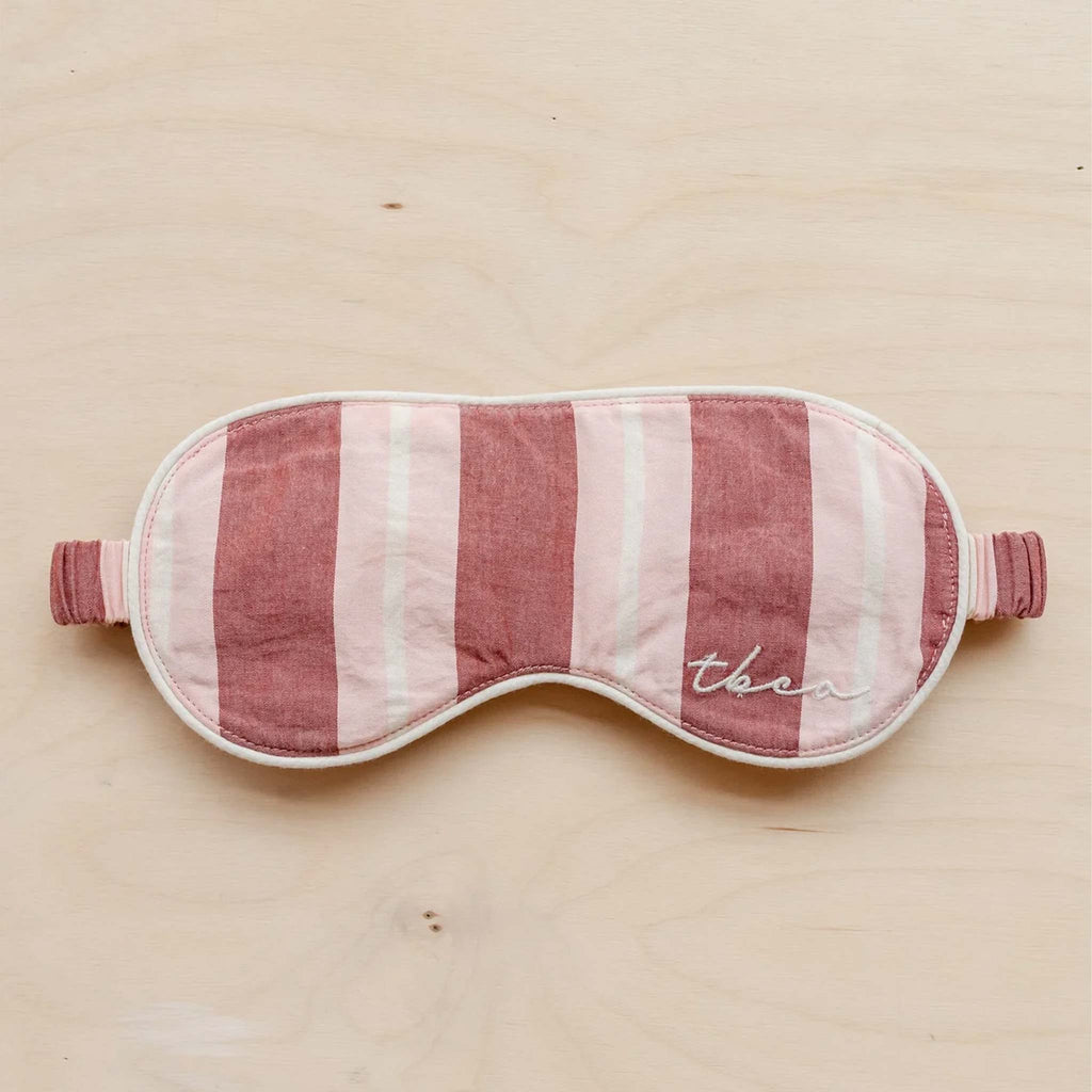 A soft, padded eye mask featuring a red, pink and cream striped pattern.