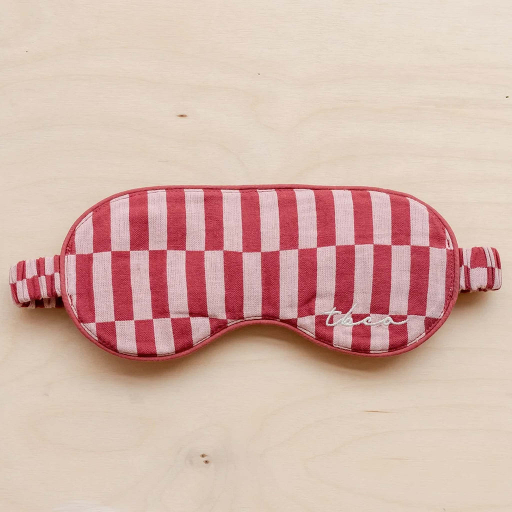 A soft, padded eye mask featuring a red and pink checkerboard pattern. 