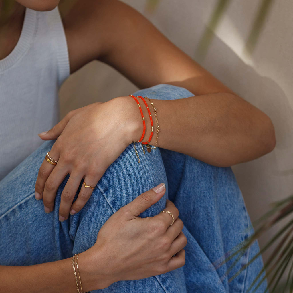 Two bright orange beaded bracelets stacked together, styled beside a minimal gold chain bracelet. 