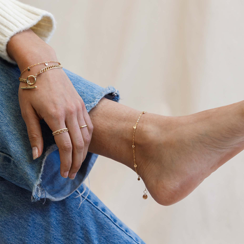 Model wears a gold charm anklet. The Telltale Anklet is a minimal gold chain, with small gold discs dangling at regular intervals. This anklet is adjustable and perfect for sunny days.