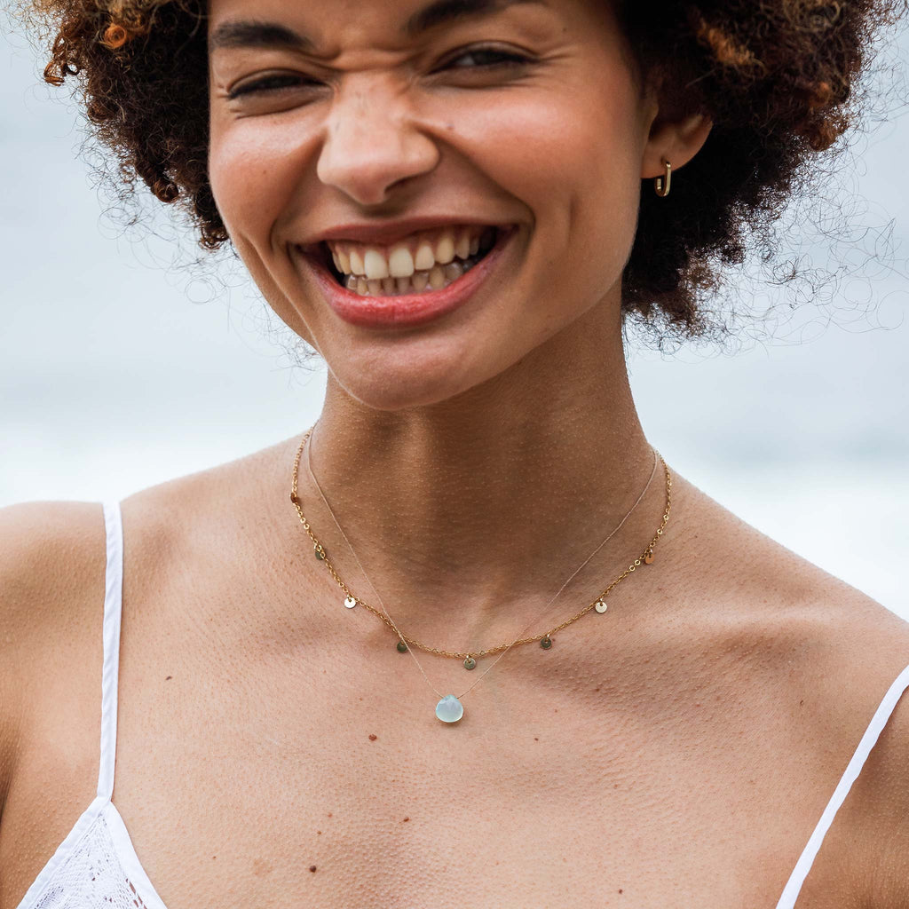 The Telltale Necklace features gold discs, hanging like charms at regular intervals. Styled with the Sea Glass Chalcedony Fine Cord Necklace.