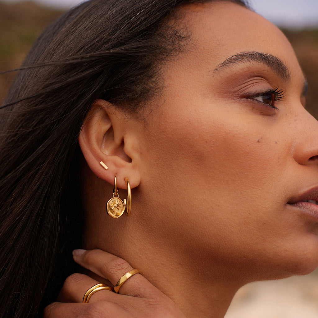 Wanderlust Life Terra Drop Hoop Earrings. New in the Elemental Collection, a hand-cast disc featuring a palm tree hangs on a gold hoop earring. The perfect summer staple to add to your ear stack. Made with recycled materials. Proudly designed in our Devon studio, and handcrafted by our Wanderlust Life global artisan partners.