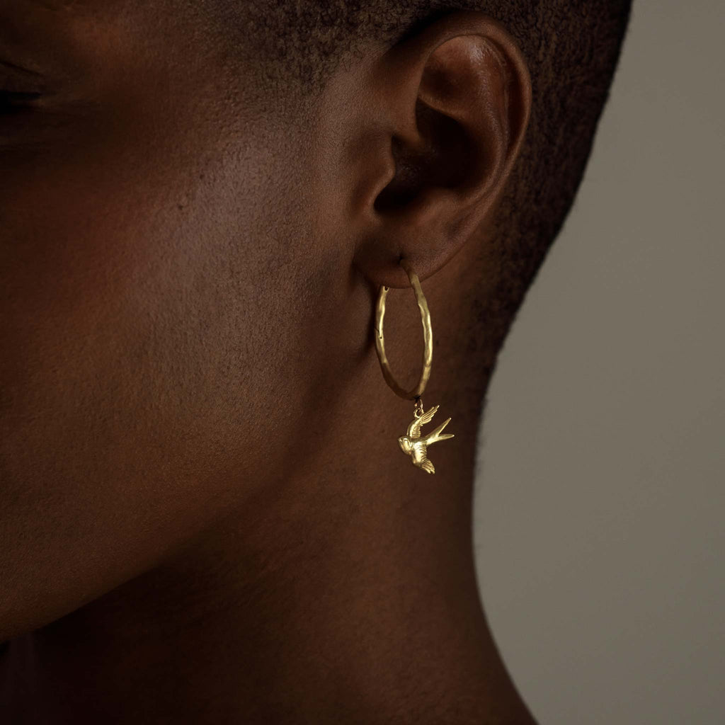 A 3-dimensional swallow charm suspends from a textured and lightly hammered hoop with a hidden hinge closure.&nbsp;