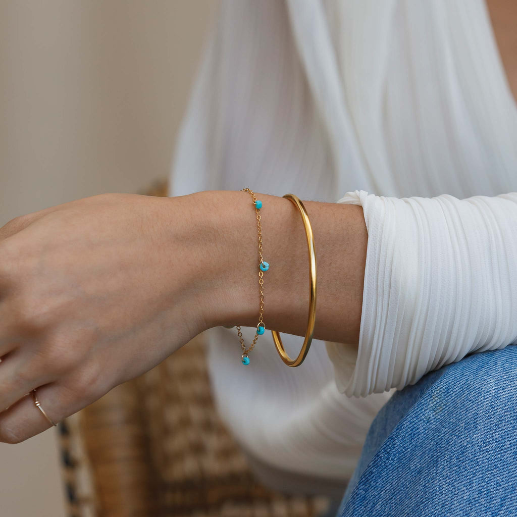 Faceted turquoise rondels are fastened at regular intervals to a minimalist gold chain bracelet. This gemstone charm bracelet is styled with a gold vermeil bangle.