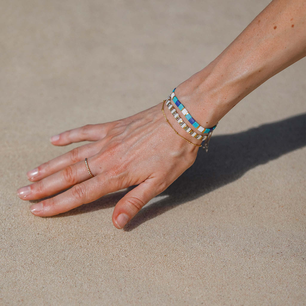 The turquoise terrazzo slider bracelet features tiled tila beads in turquoise, royal blue, white and gold. Styled in a bracelet stack with the gold terrazzo slider bracelet and satellite chain.