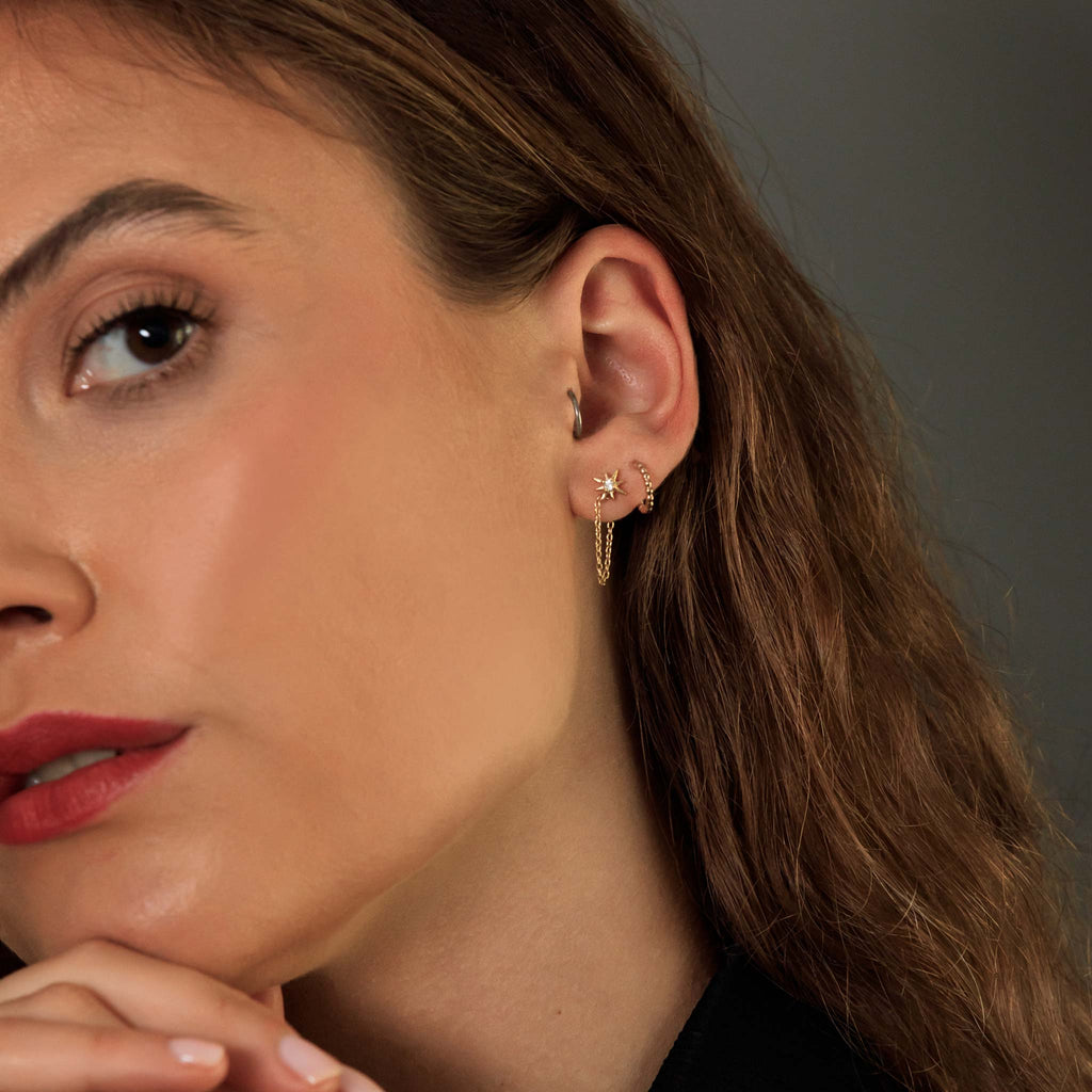 A white topaz stud earring connects to its backing with a dainty gold chain, that add movement and energy to your ear stack.