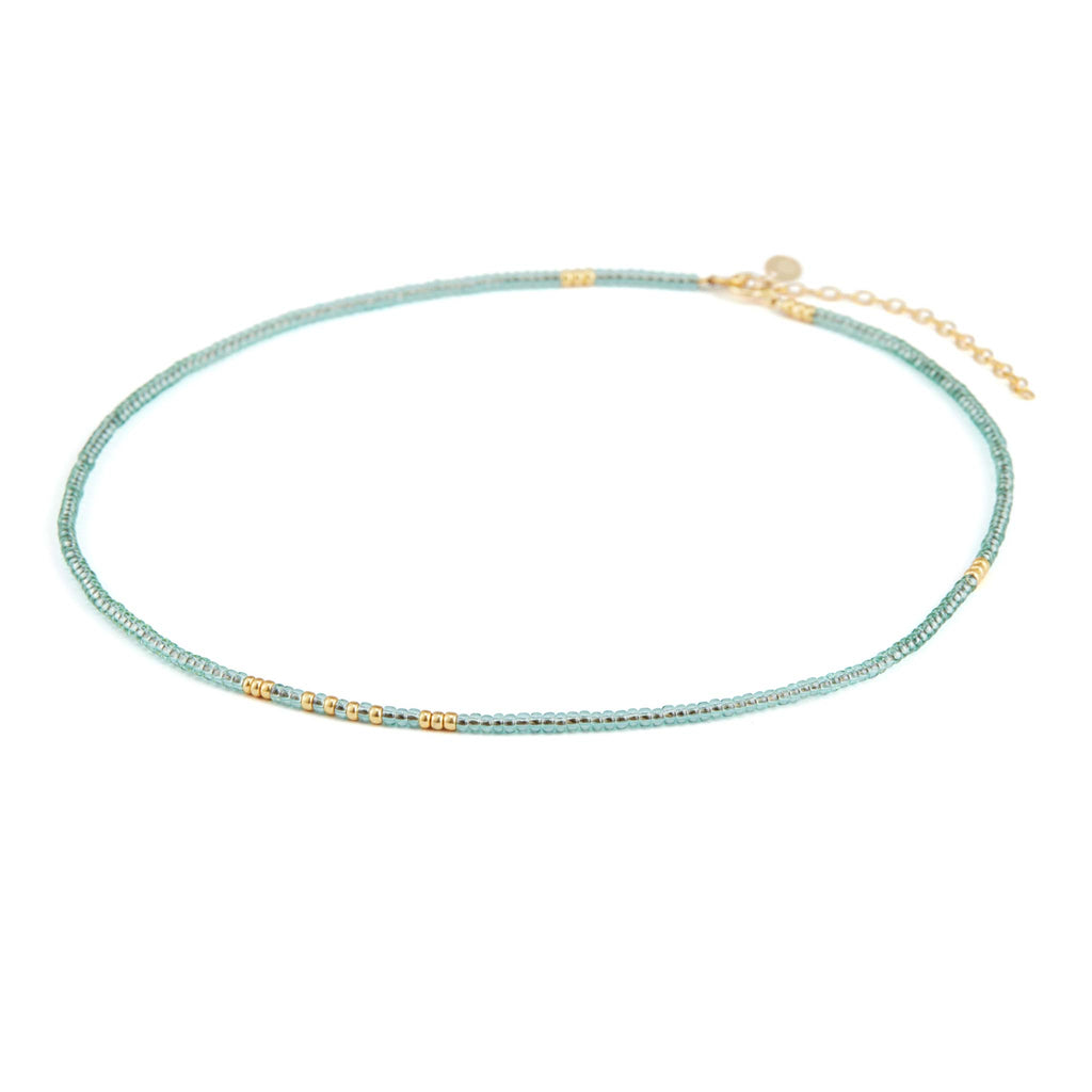 The water blue beaded necklace features translucent beads in a pale blue, reflective of water. There are flecks of gold beads throughout the necklace, creating an irregular pattern. The necklace is finished with 2 inches of chain, making this choker style necklace an adjustable length.