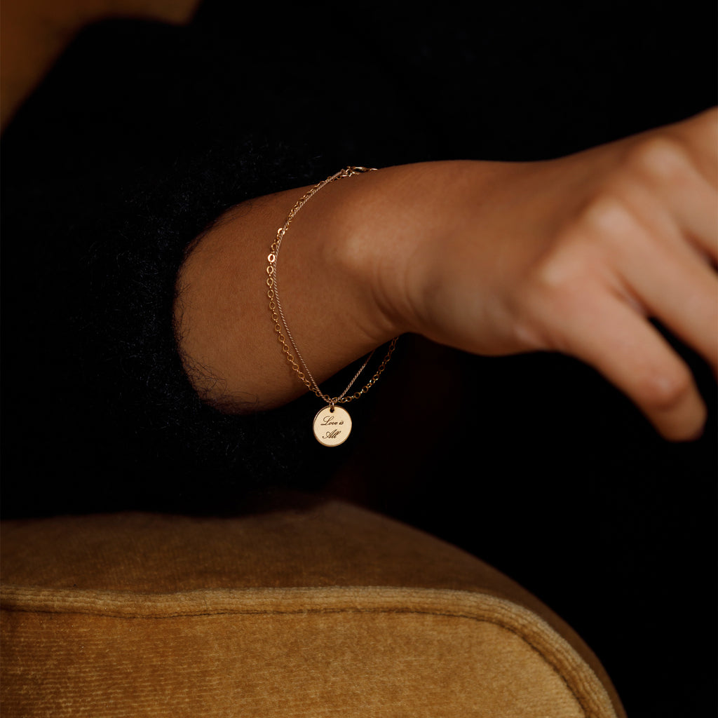 Charged with meaning, an engravable disc slides on a delicate bracelet of gold and silk. You can engrave on one or both sides with complimentary engraving.