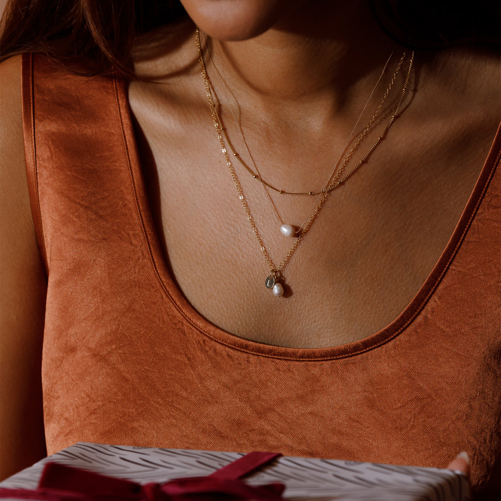 Satellite chain necklace layered with the pearl fine cord necklace and the pearl pendant necklace with a handstamped initial tag.