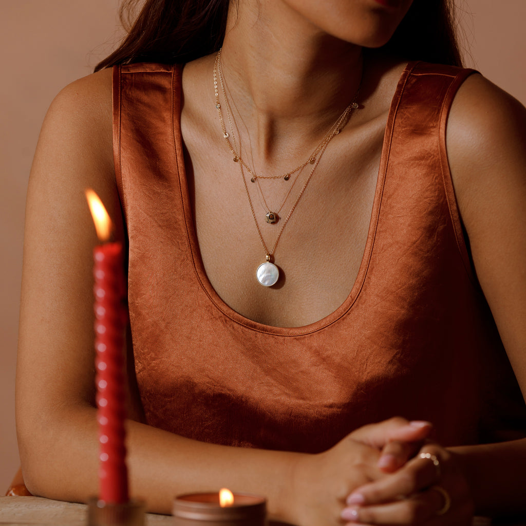 A gold necklace stack of telltale chain necklace, leopard jasper fine cord necklace and mother of pearl porthole necklace.
