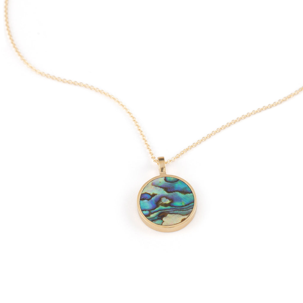 A Porthole Necklace with a circular slice of Paua shell, framed in brushed gold vermeil pendant. Styled with a mother of pearl beaded necklace.