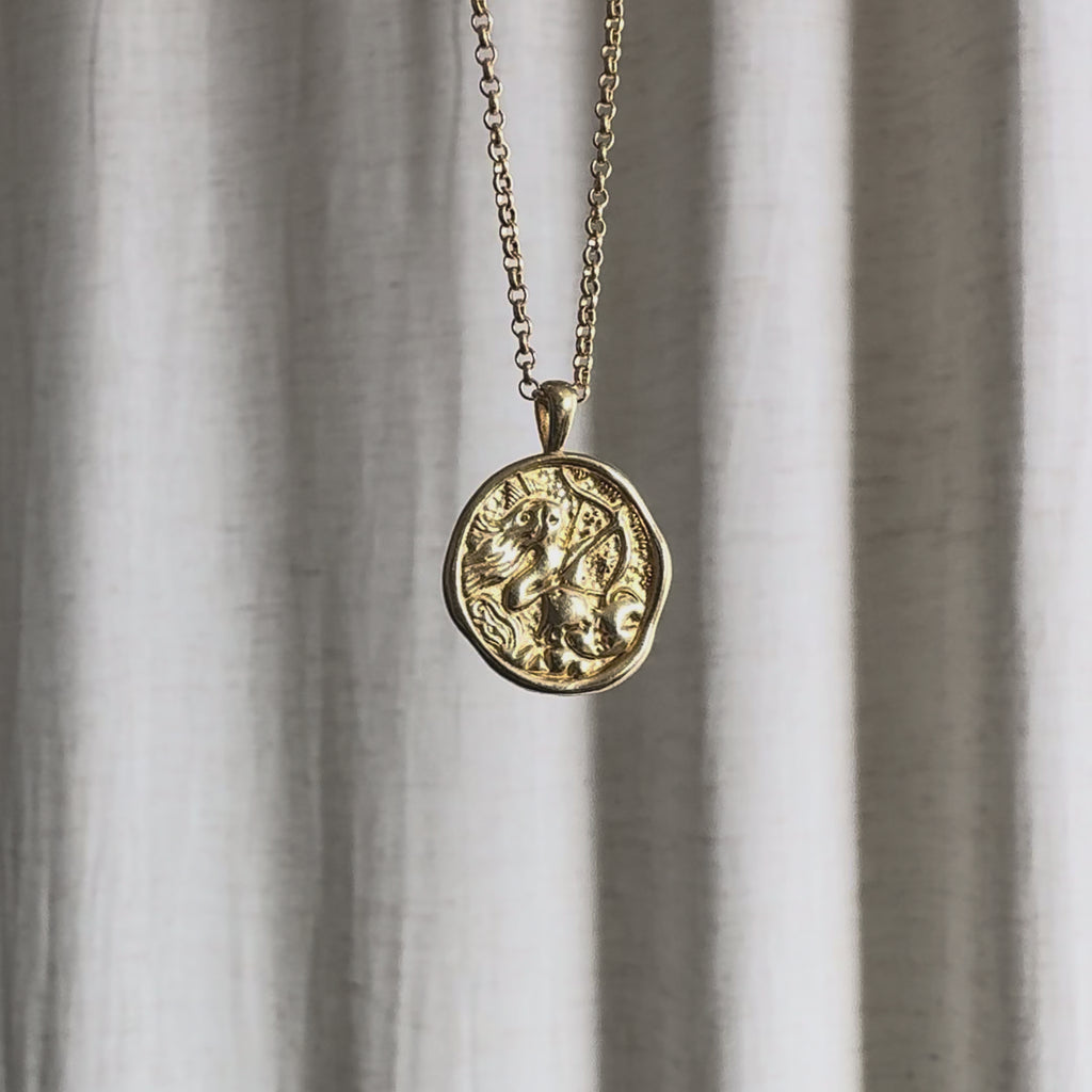 Video of Sagittarius Zodiac Pendant Necklace moving in the sun against a natural fabric background.