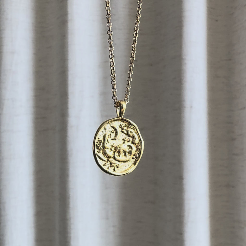 Video of Cancer Zodiac Pendant Necklace moving in the sun against a natural fabric background.