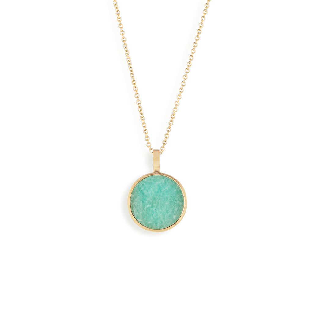 A circular pendant features a gemstone slice of Amazonite, featuring turquoise hues and a texture reminiscent of the ocean. The pendant hangs on a minimal gold fill chain.