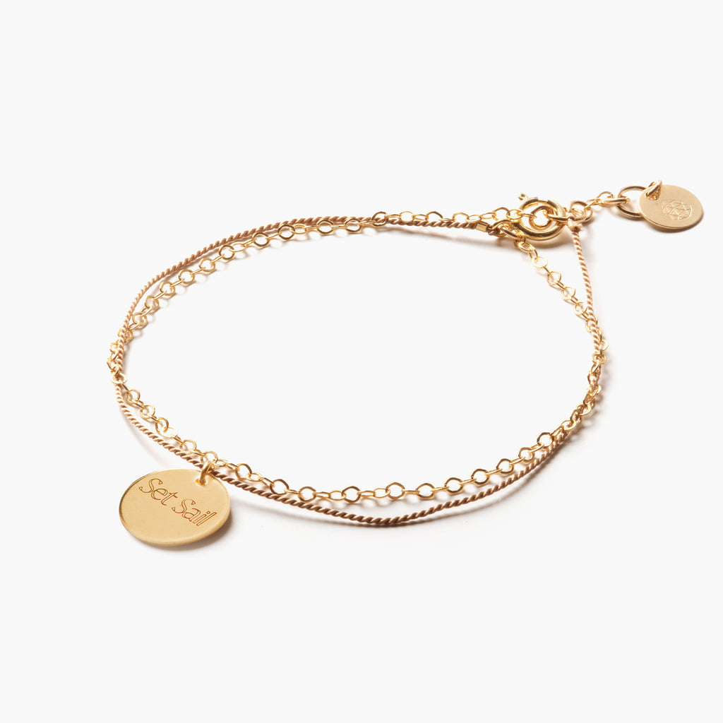 Engraved with the phrase 'set sail', the Insignia Gold and Silk Bracelet is an affordable engravable bracelet. Engrave the disc charm on the back and front with a completely custom engraving like a date, name, mantra or combination. 